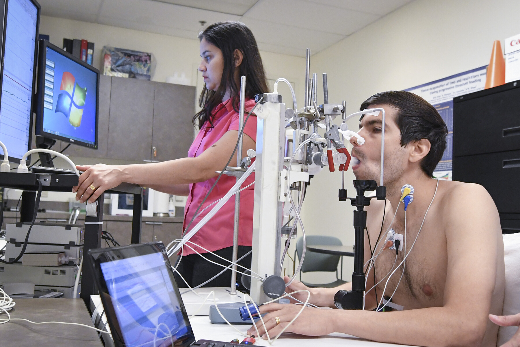A man and a woman in a lab. He is taking a test and she reading the results on a monitor