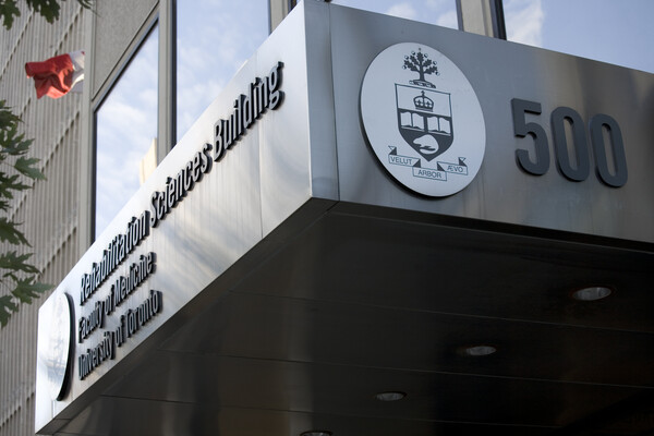 Picture of the overhang of the Rehabilitation Sciences Building from the corner, showing the name of the building along one edge and the crest with the address number along the right edge of the corner.