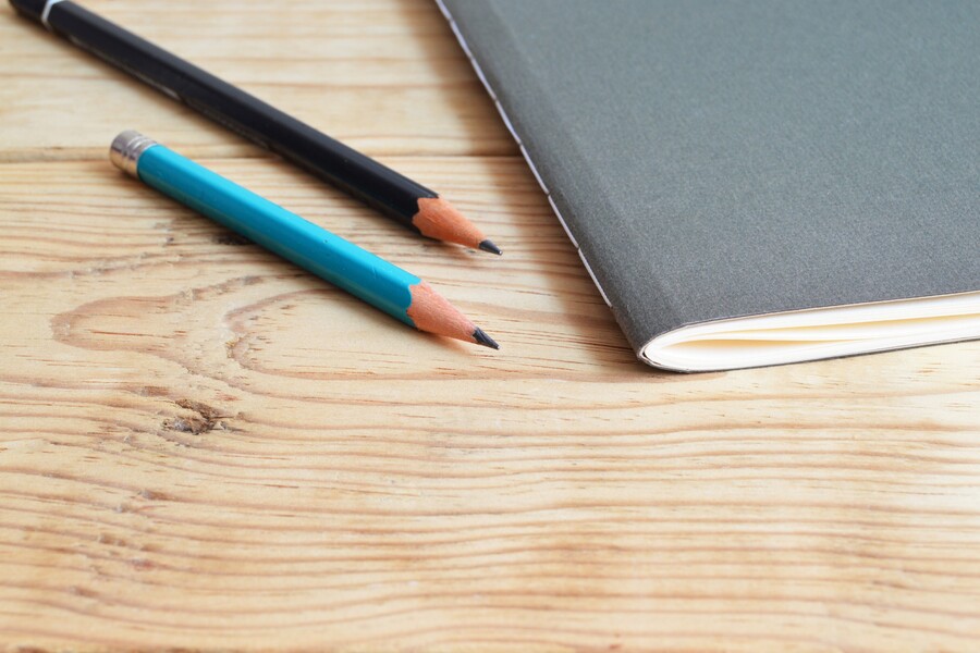 two pencils and a grey notebook sit on a wooden table