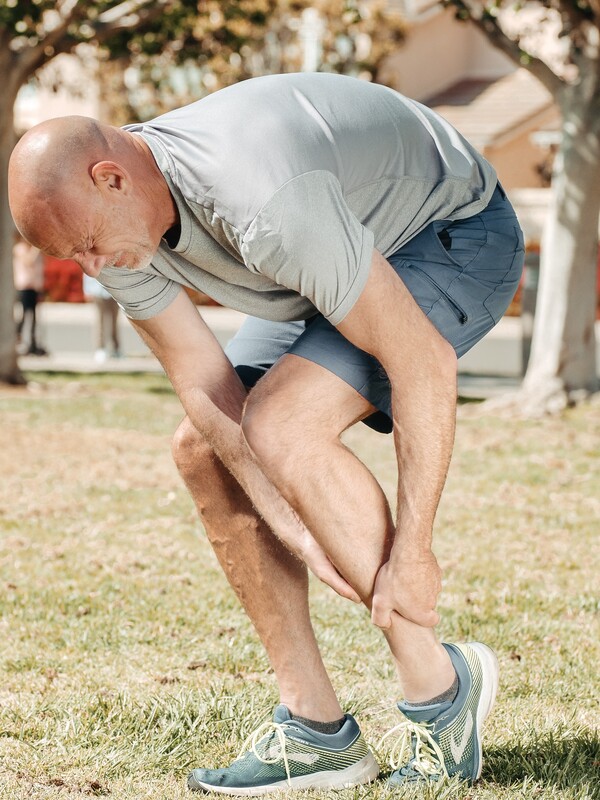 older person crouching down holding their lower leg in pain